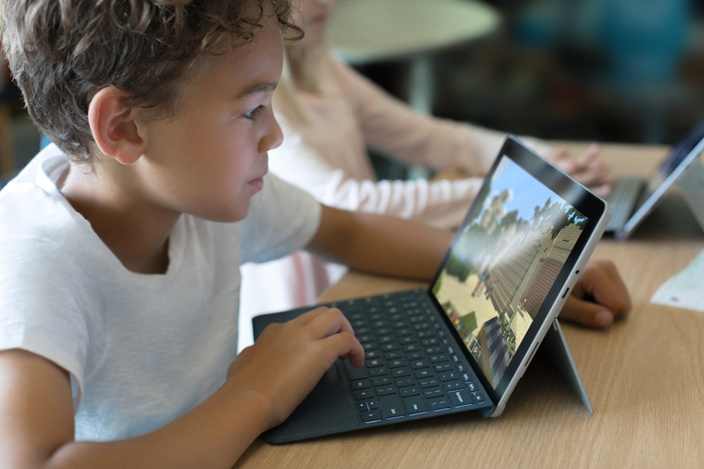 Ein Grundschüler sitzt vor einem Surface. Ein kleiner Junge sitzt vor einem Surface