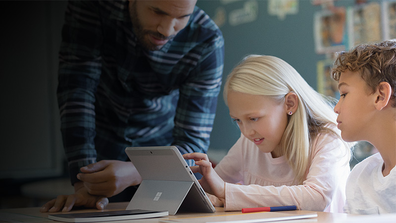 Ein Lehrer hilfe einer Sch&uuml;lerin beim Arbeiten an einem Surface Laptop