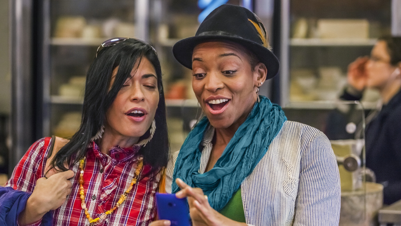 Zwei Frauen schauen erfreut auf ihr Smartphone