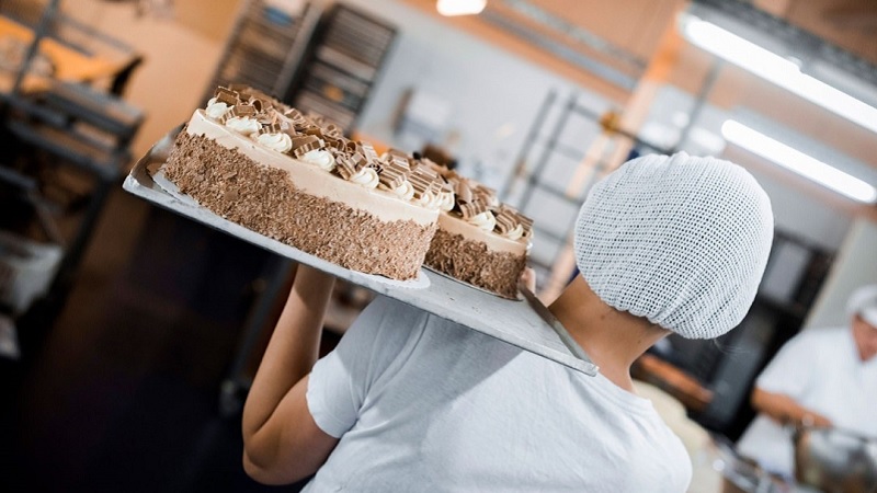 Eine Konditorin, von hinten fotografiert, tr&auml;gt eine Sahnetorte