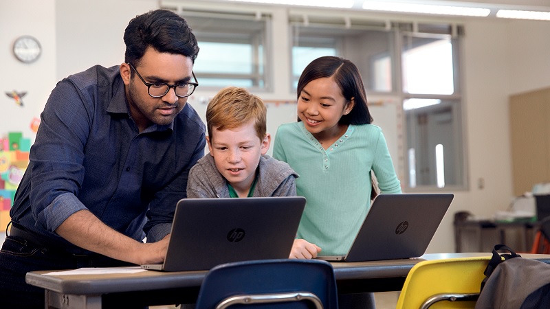 Ein Lehrer, ein Junge und ein M&auml;dchen schauen gemeinsam auf einen Laptop