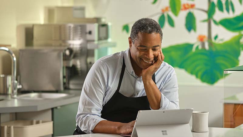 Mann in einer Kochsch&uuml;rze steht in einer Restaurantk&uuml;che und blickt auf ein Surface Laptop Pro