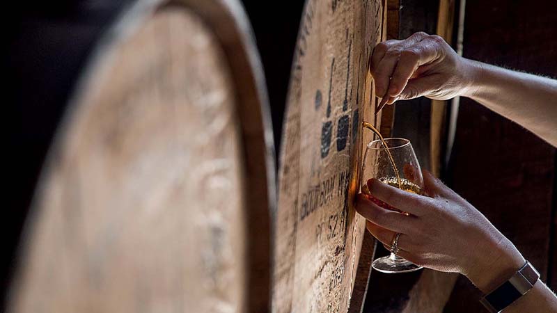 Jemand entimmt eine Probe aus einem Whiskey Fass