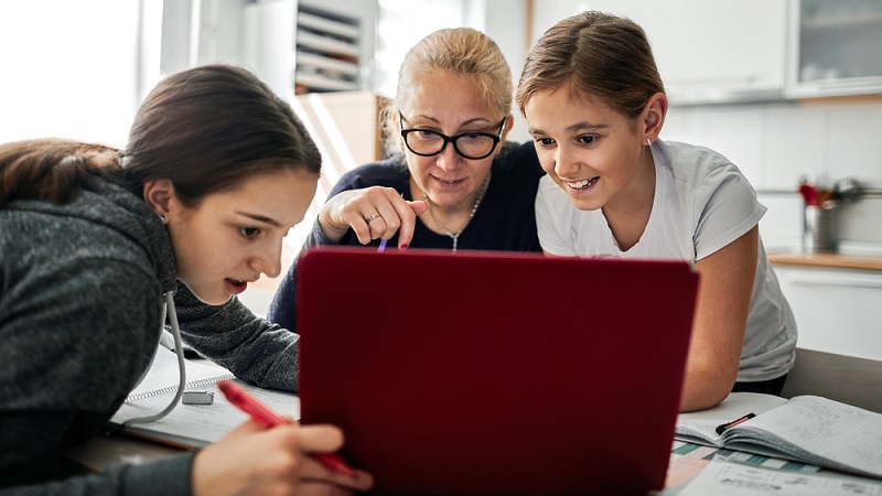 Mutter hilft ihren T&ouml;chtern, die Hausaufgaben w&auml;hrend der Coronavirus-Quarant&auml;ne zu erledigen. Sie benutzen Laptop