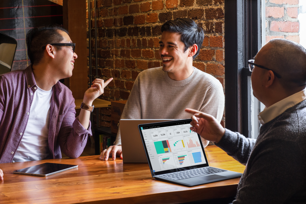Three coworkers sitting at a table talking over a Microsoft Surface laptop