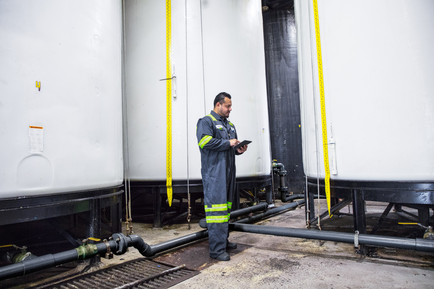 Male worker wearing utility suit using tablet. Industrial vats visible in background