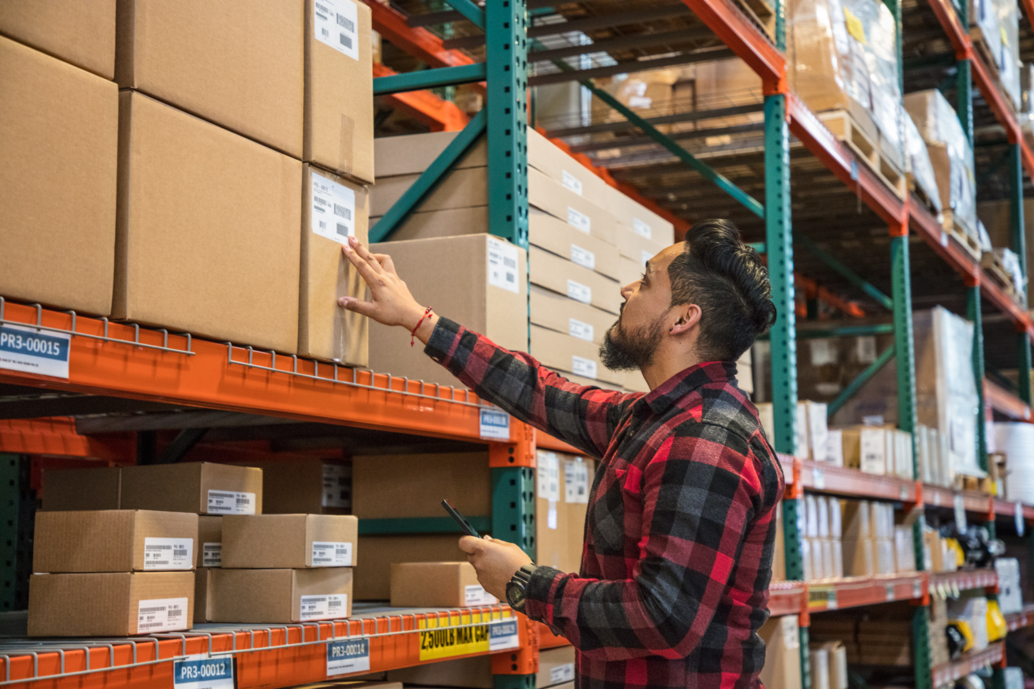 Male worker using phone and checking boxes in warehouse. Phone screen not visible