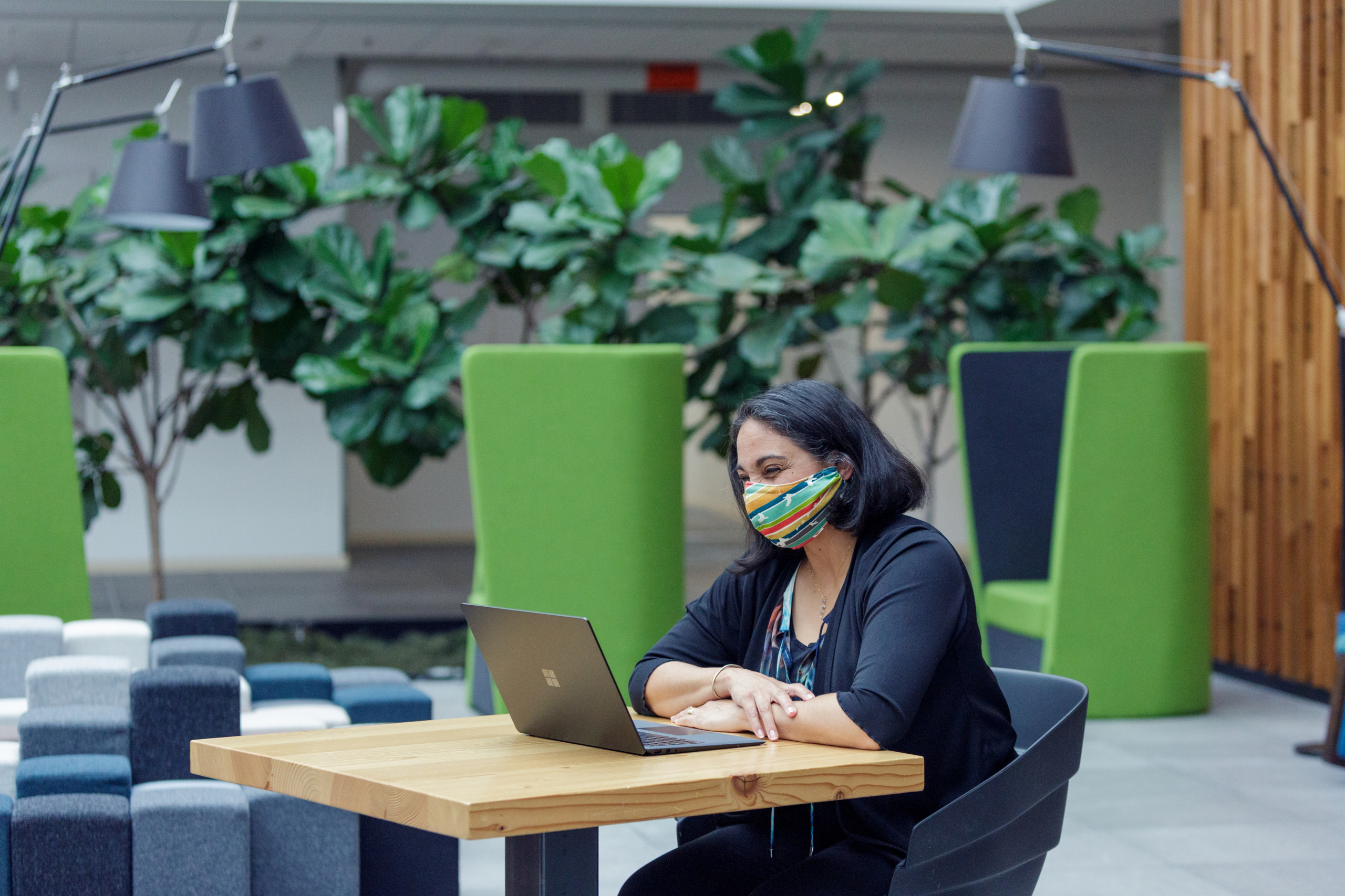 A female employee working on her Surface laptop wearing a mask and smiling