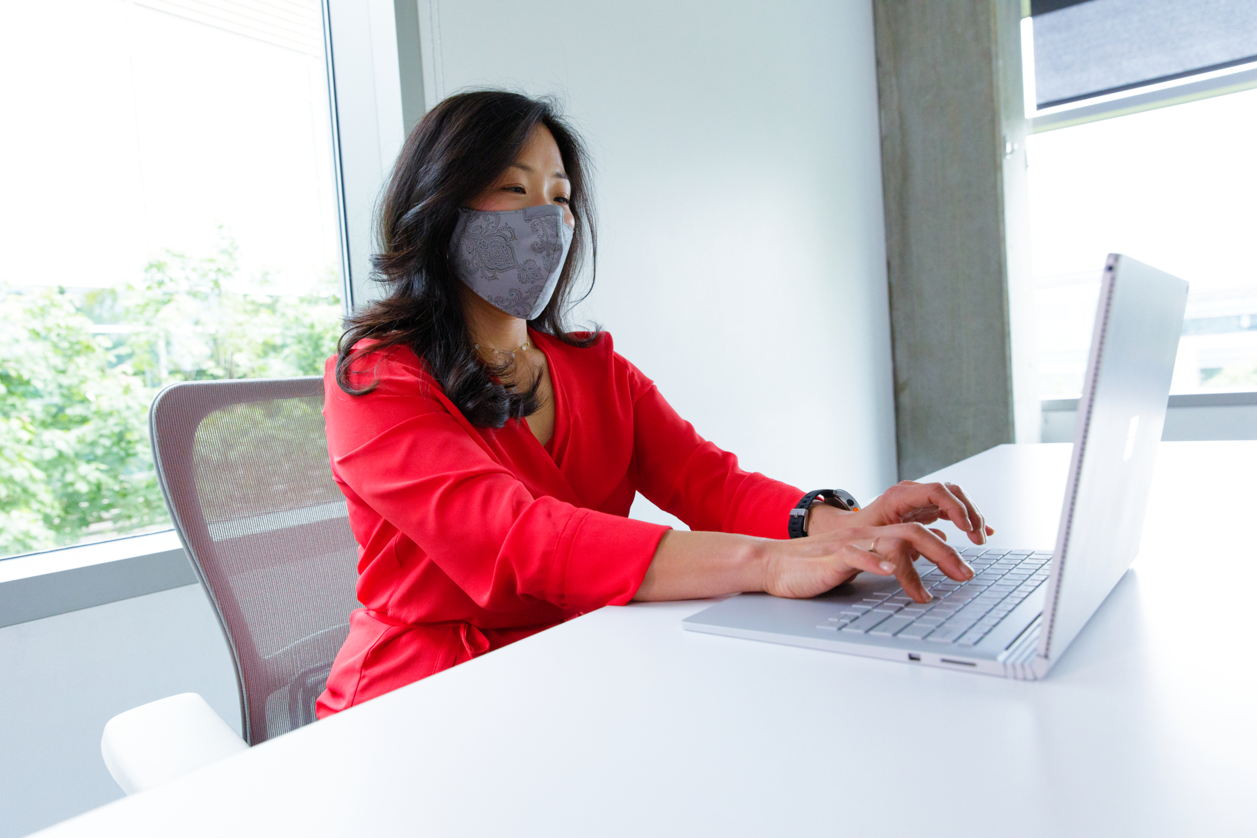 A female employee wearing a face mask and working on her Surface Book laptop at her desk. Hybrid Workplace collection