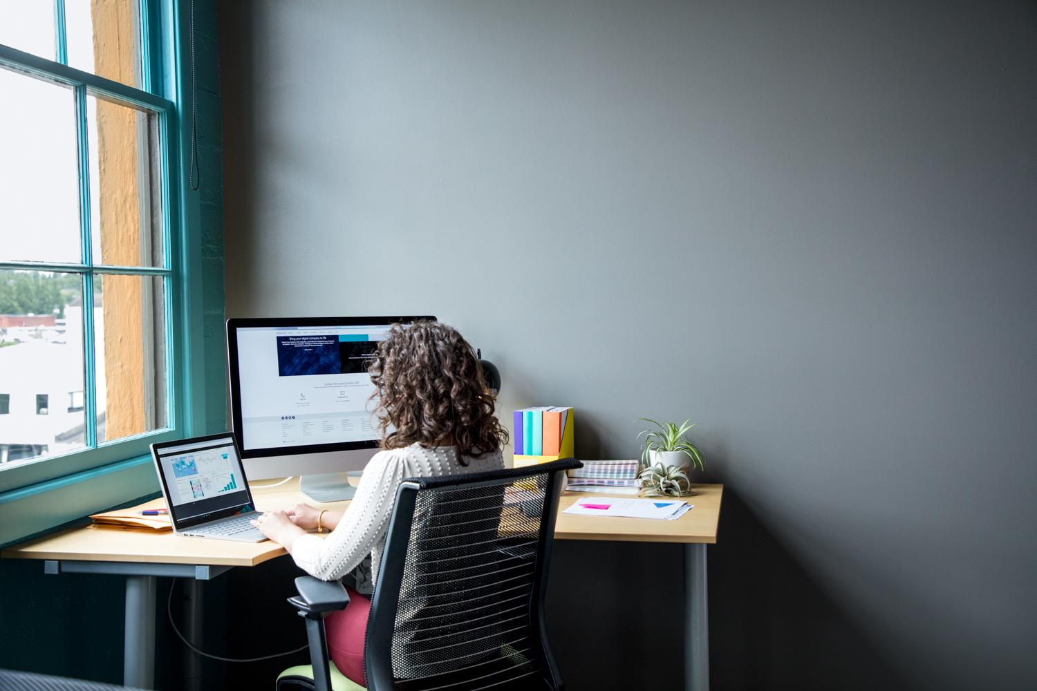 Female office worker sitting at desk using Surface Laptop in casual office setting