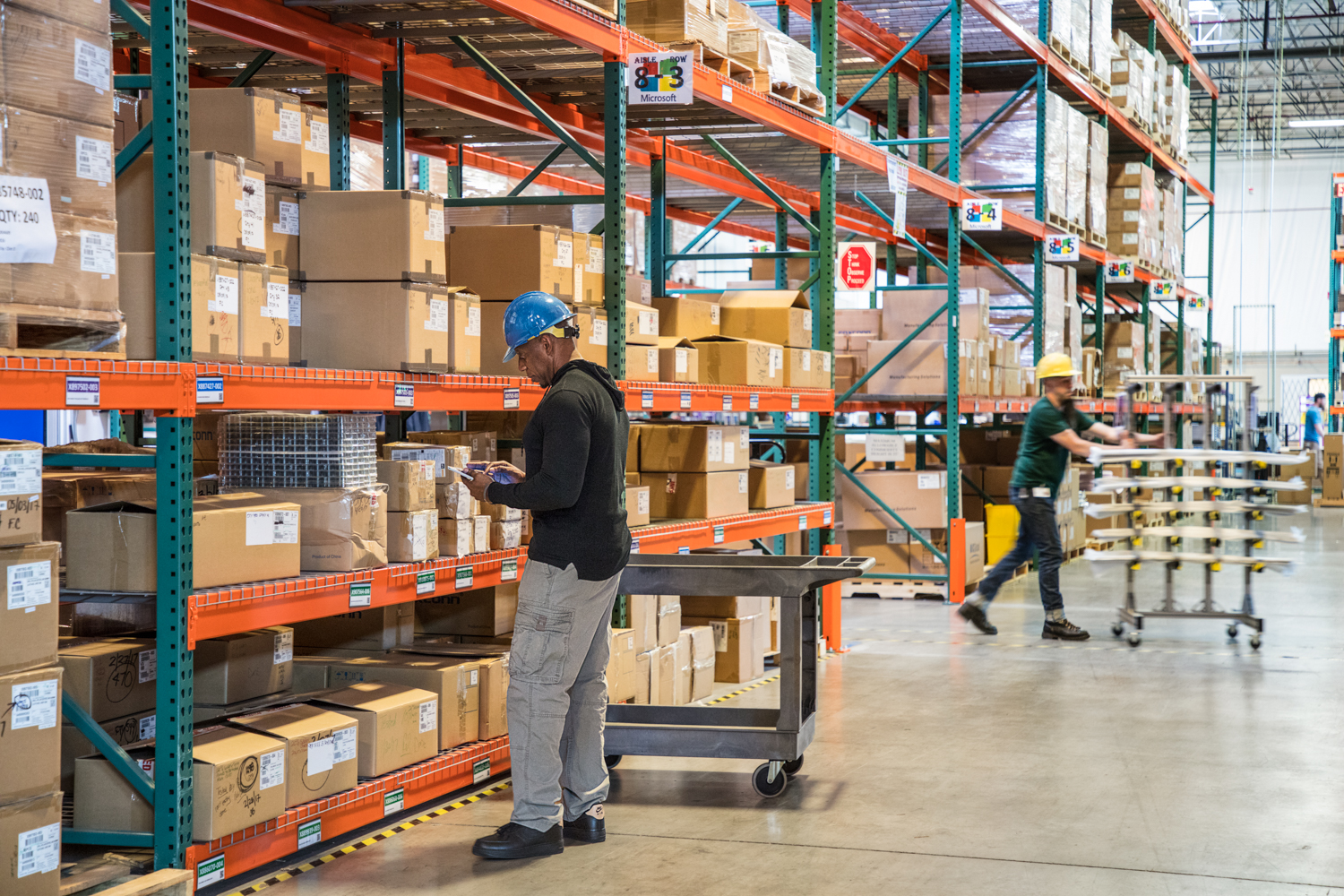 Male worker wearing hardhat using tablet in warehouse. Another worker in background