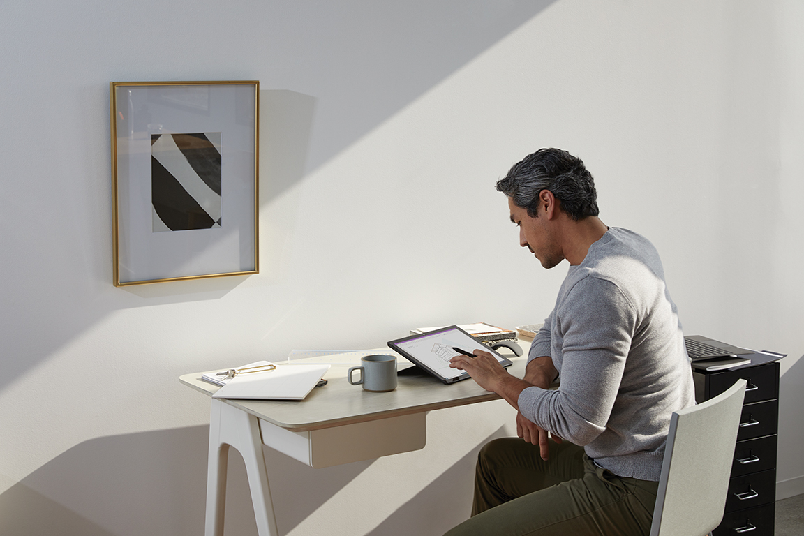 Adult male in home office environment using Microsoft OneNote at a desk with a black Microsoft Surface Pro 7 in studio mode