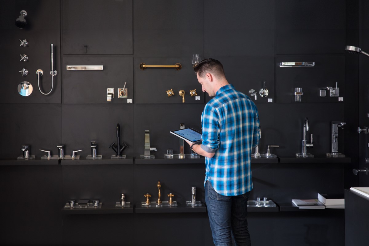 Male millenial using Surface Pro and Surface Pen, standing in front of faucet display wall in a kitchen and bath showroom
