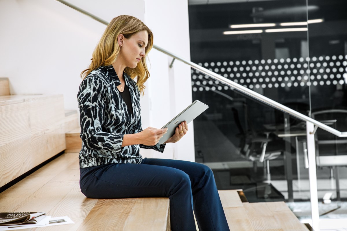 Woman sitting on steps in open office building. She is using a tablet