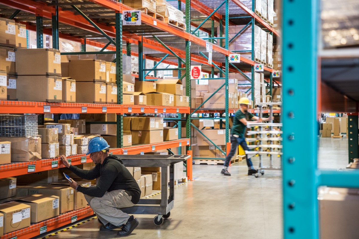 Male worker wearing hardhat using tablet in warehouse. Another worker in background