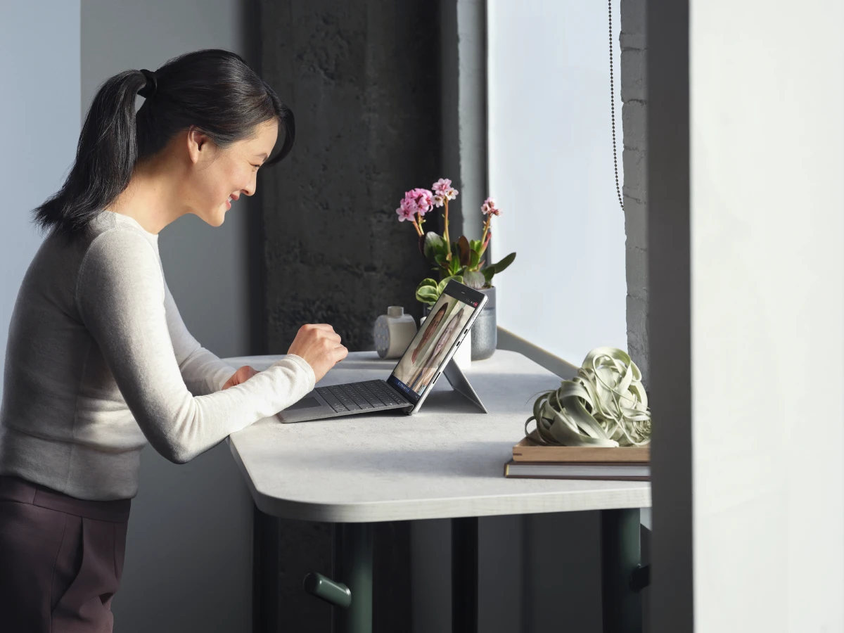 Adult female standing at her desk collaborating via Microsoft Teams video call on a Surface Pro 8 in laptop mode working on a Surface Pro Signature Keyboard