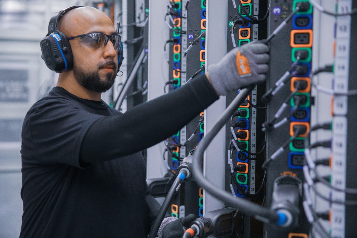 Male datacenter employee plugs cable in hot aisle power distribution unit