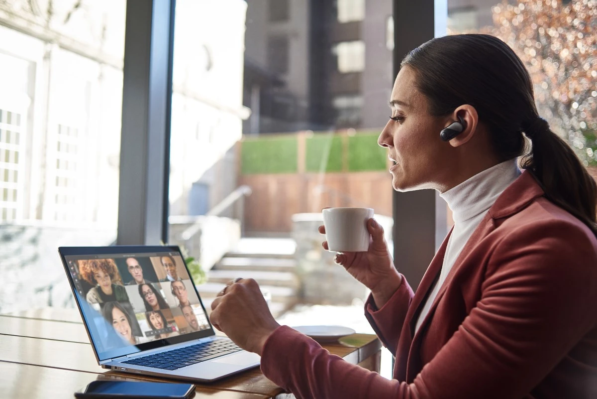 Female small business executive using HP Elite device running Microsoft Teams conference call. Different screens are available: one featuring 1 person on screen, another with 9 people on screen. Keywords: Microsoft Teams, Bluetooth, coffee