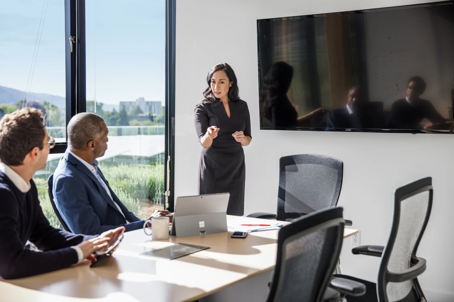 Female corporate executive giving speech to two male coworkers at conference room table in corporate office