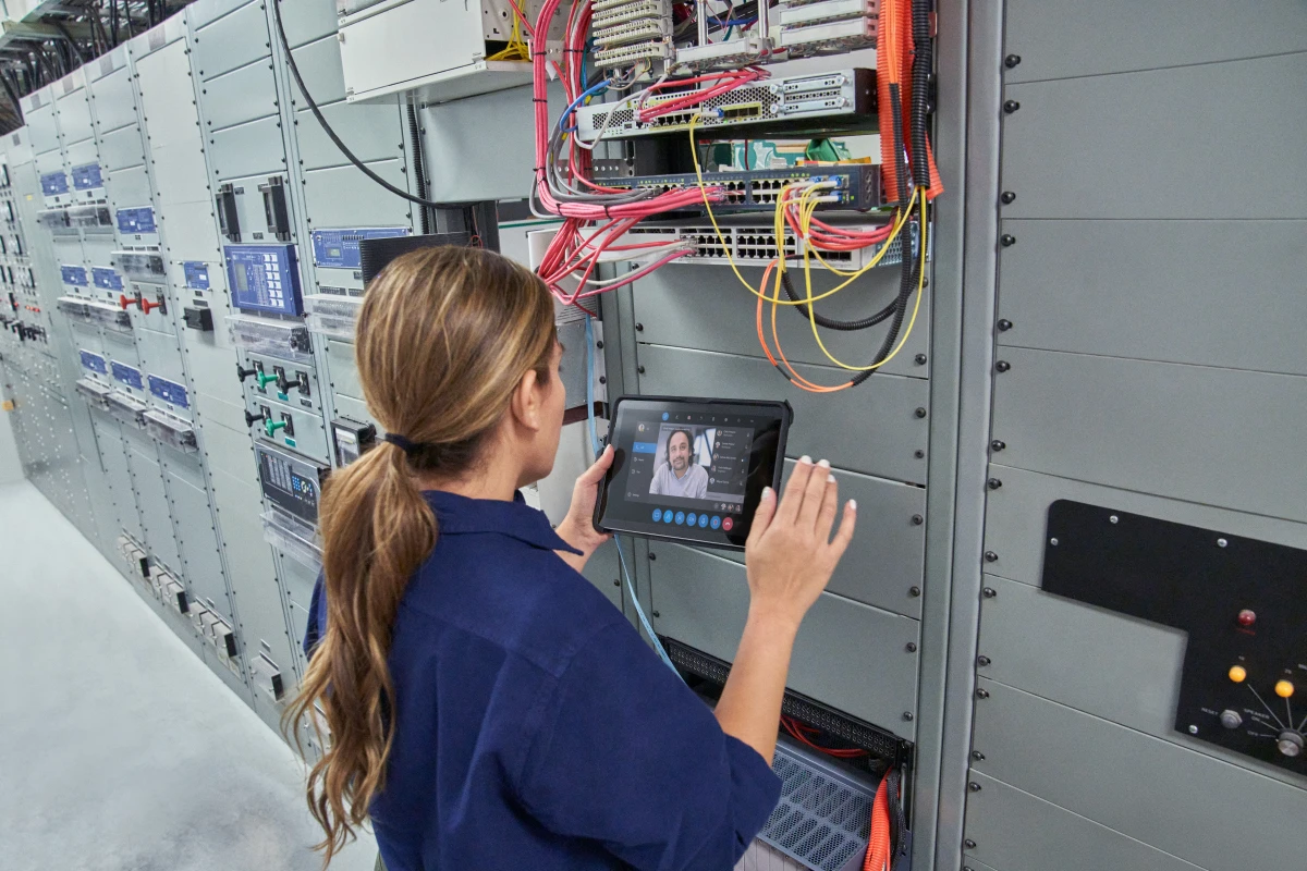 Field engineer inspects electrical substation server room on a wind farm using remote assist with a Surface tablet