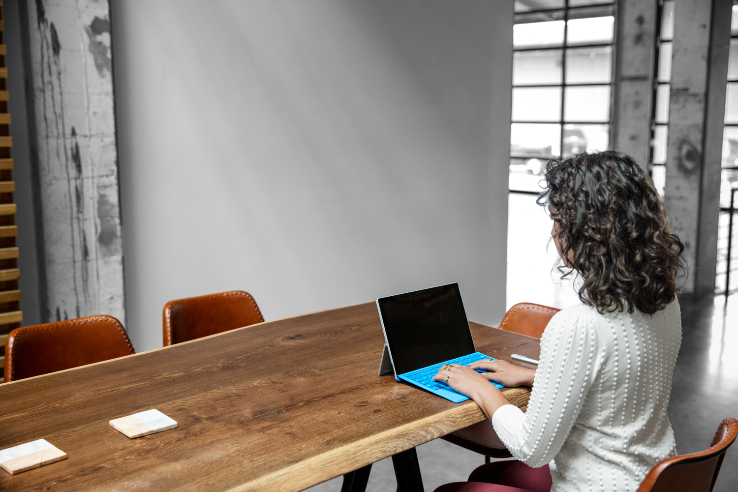 Photo looking over shoulder of female worker using computer in casual open office setting
