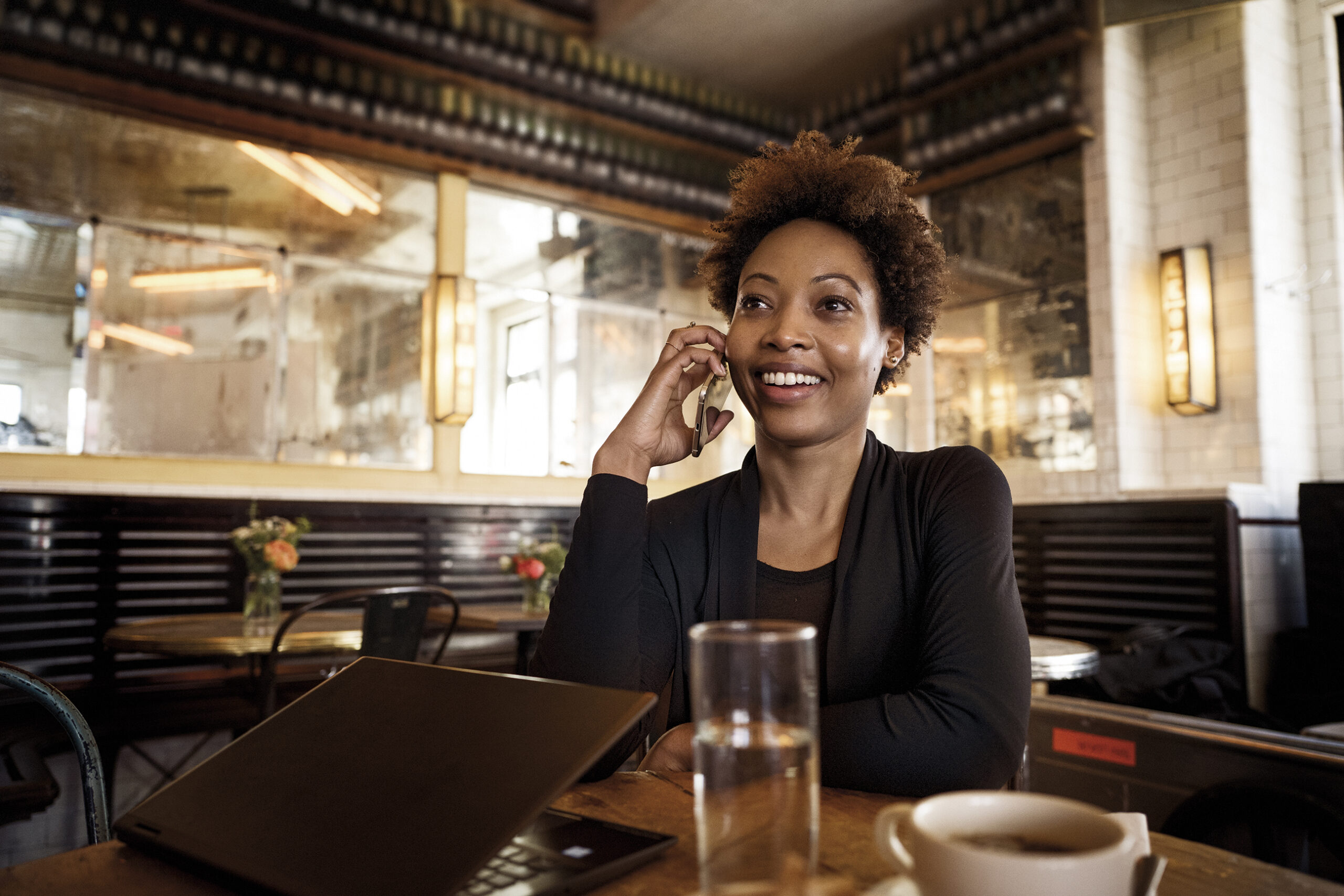 Photo of a young woman smiling while talking on the phone in a cafe
