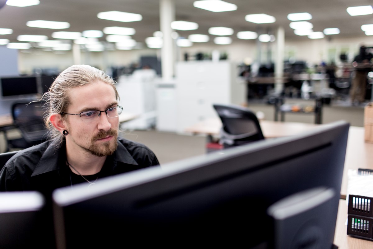 Male worker sitting at desk in manufacturing office and looking at two monitors (screens not shown)