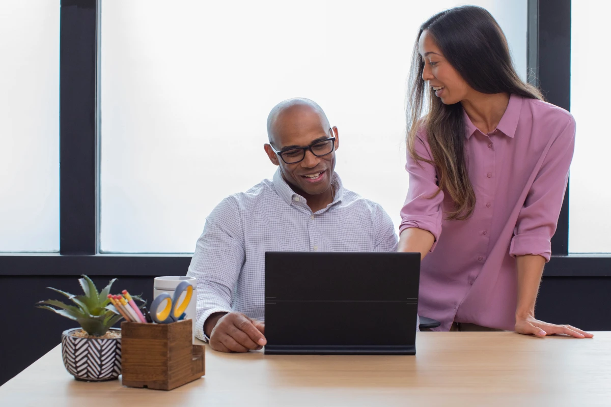 Man sitting at desk in a small business office with an HP Elite Folio, which is a commercial device, collaborating with woman standing