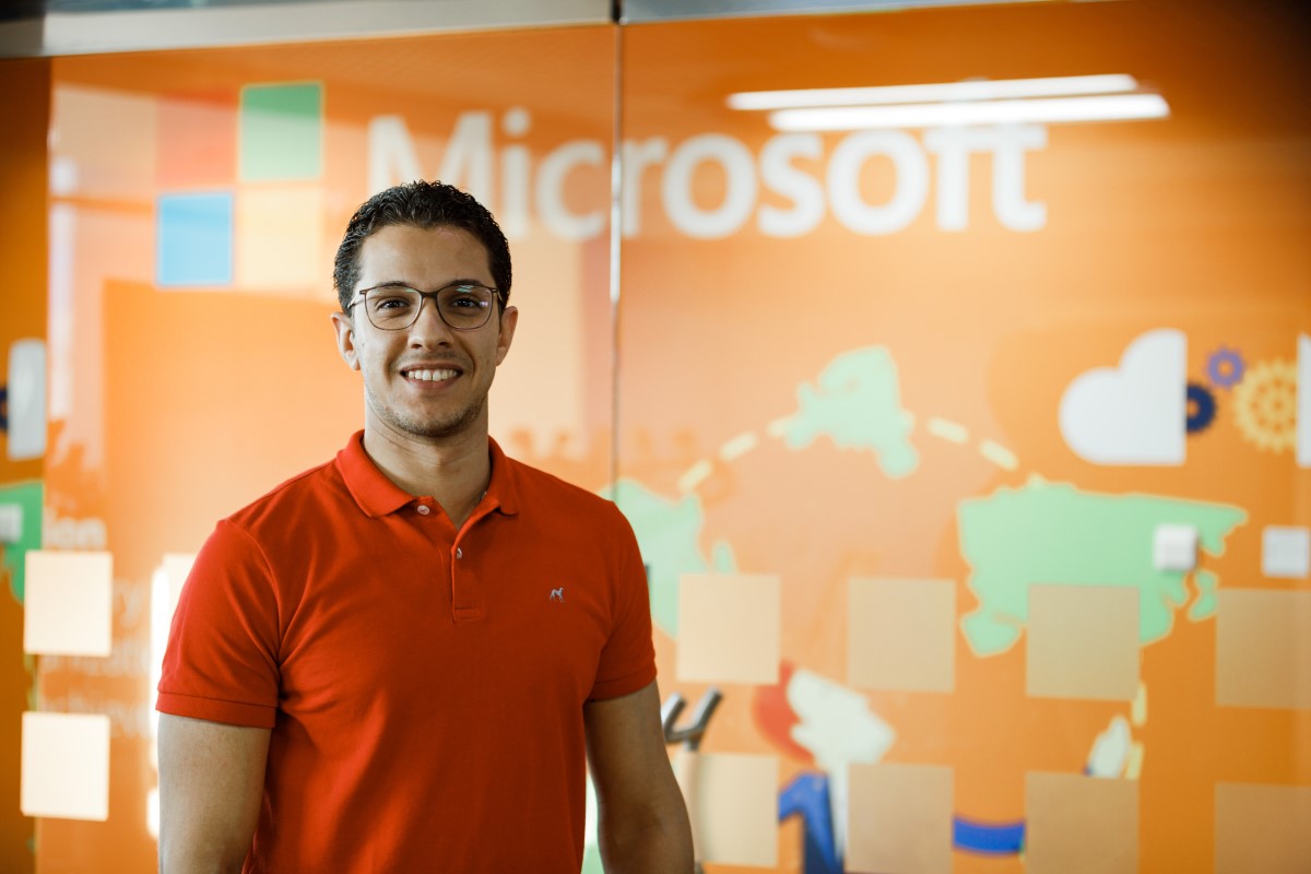 Close up portrait of male office worker standing in front of Microsoft wall display, smiling and looking directly at camera