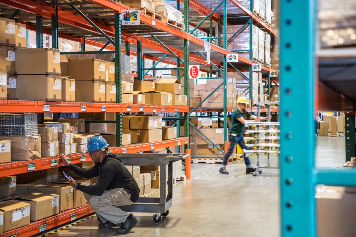 Male worker wearing hardhat using tablet in warehouse. Another worker in background
