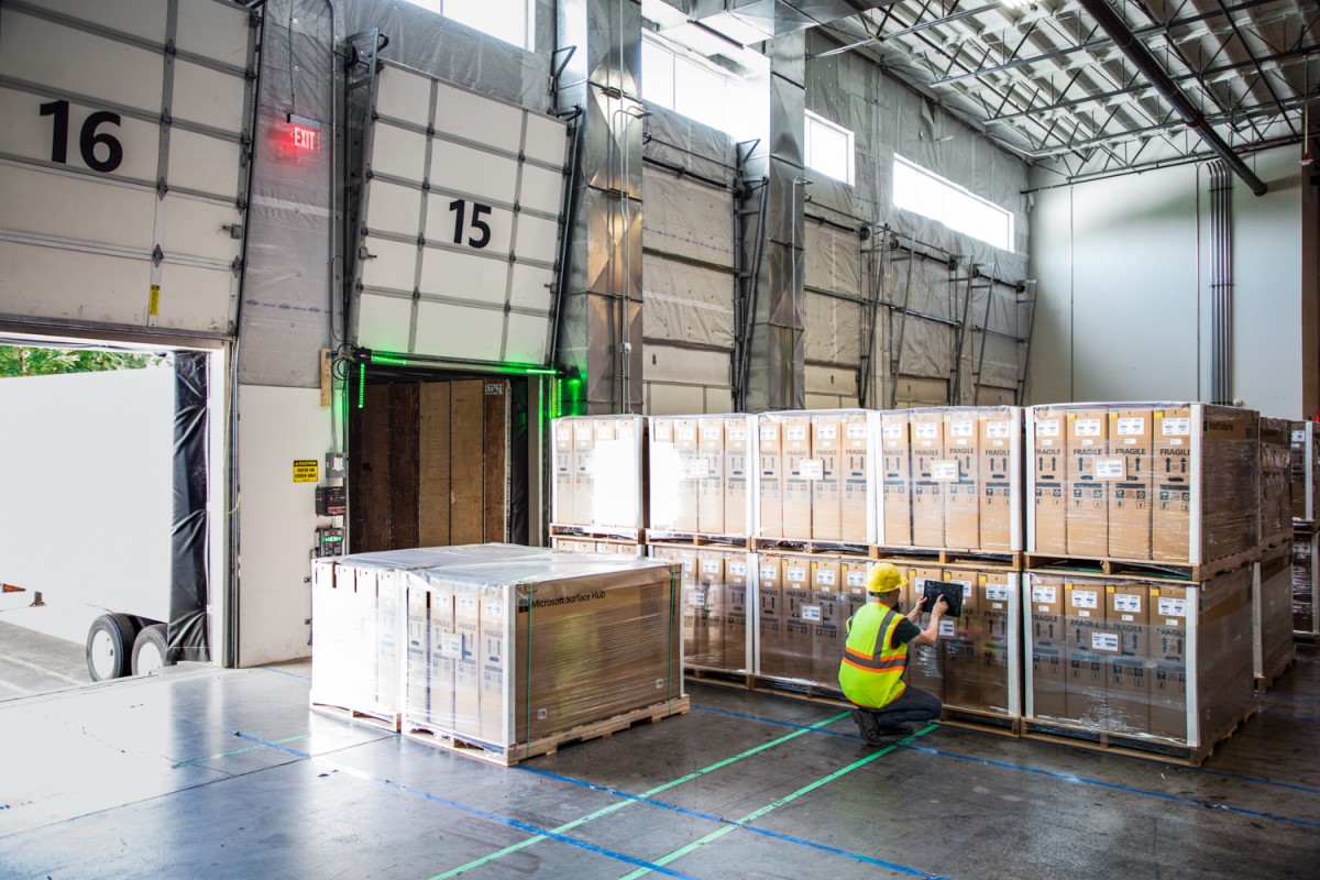 Worker in hardhat and reflective vest using tablet in warehouse loading dock