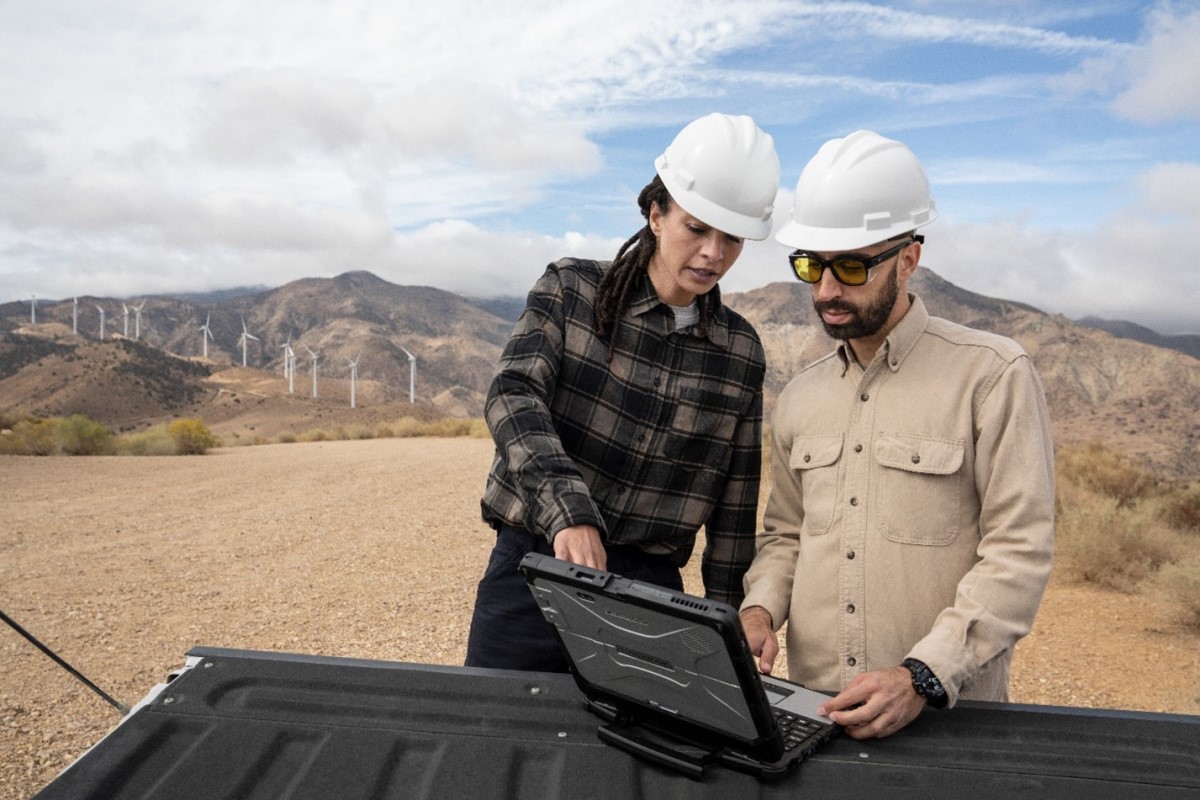 Two people, outside, looking at a laptop that is sitting on an open truck bed