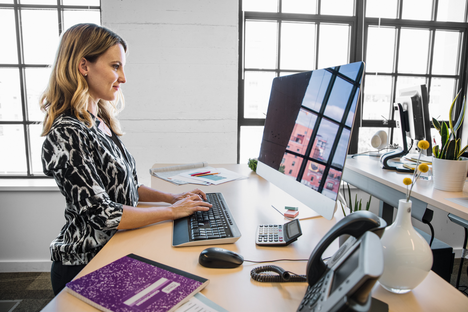 Female office worker standing at desk using desktop computer. Blank screen shown