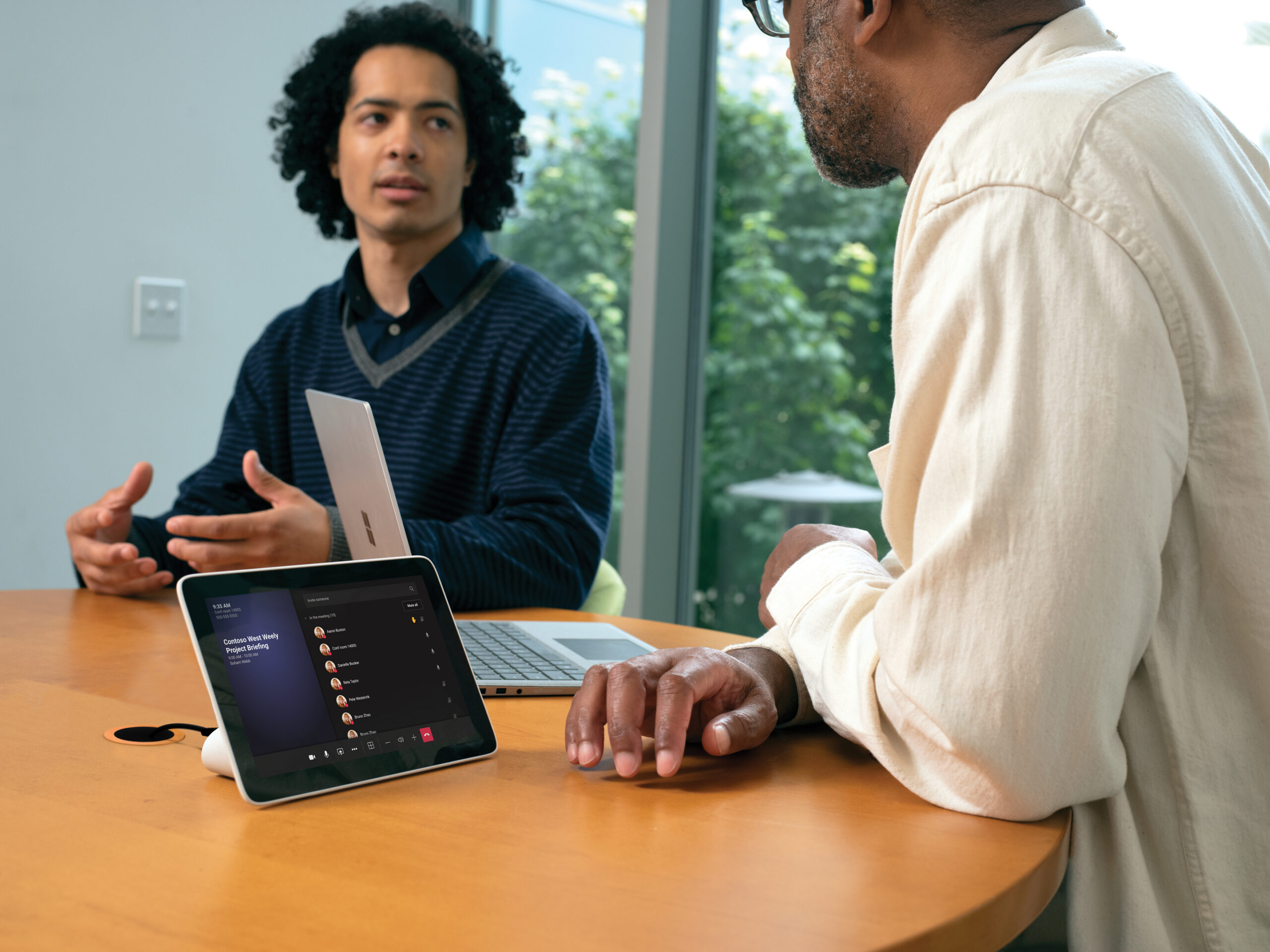 Two males in small conference room with a Poly Microsoft Teams Rooms on Android touch display in a Teams Meeting and one Surface laptop in view