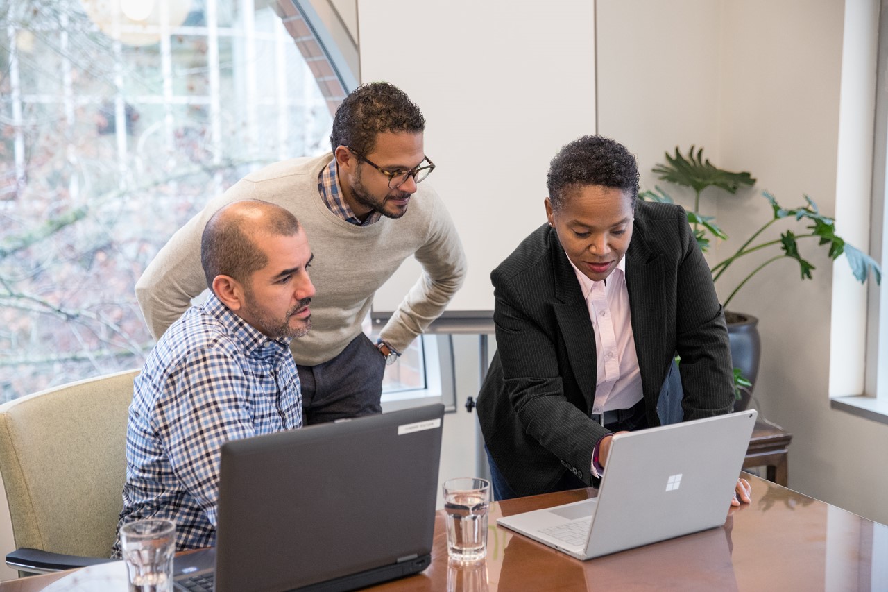 Three people at a conference table, looking at a laptop