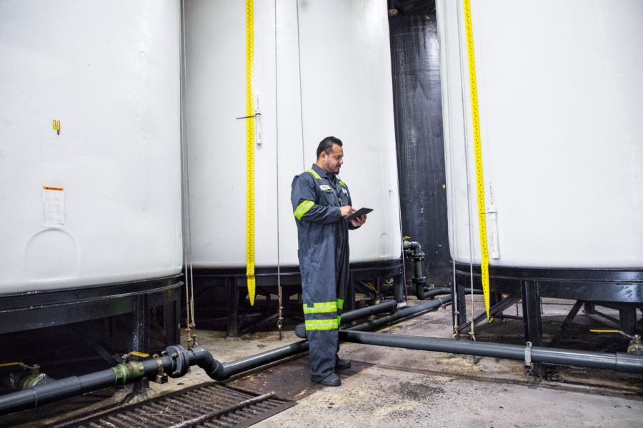 Male worker wearing utility suit using tablet. Industrial vats visible in background