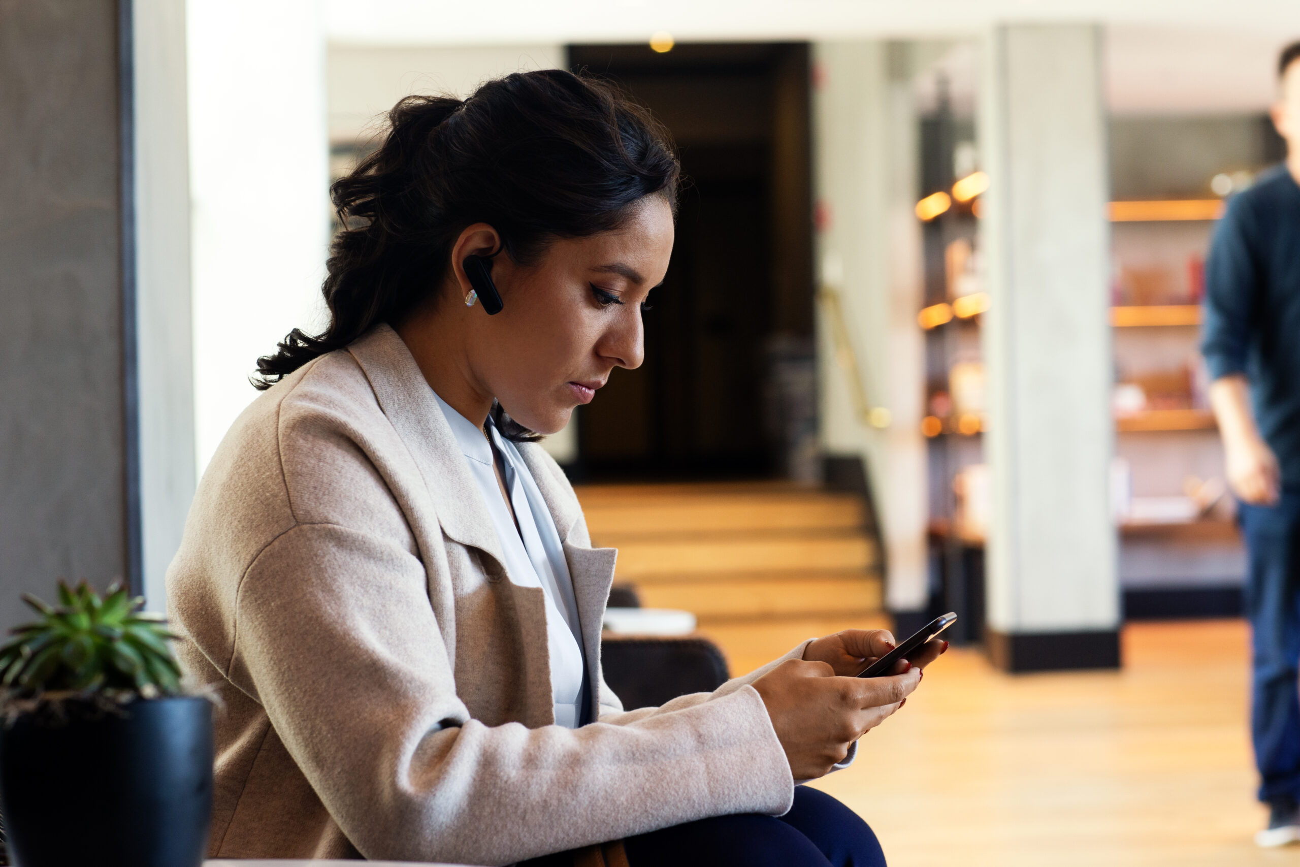 Photo of a female manager sitting in a hotel lobby approving a purchase order on her mobile device
