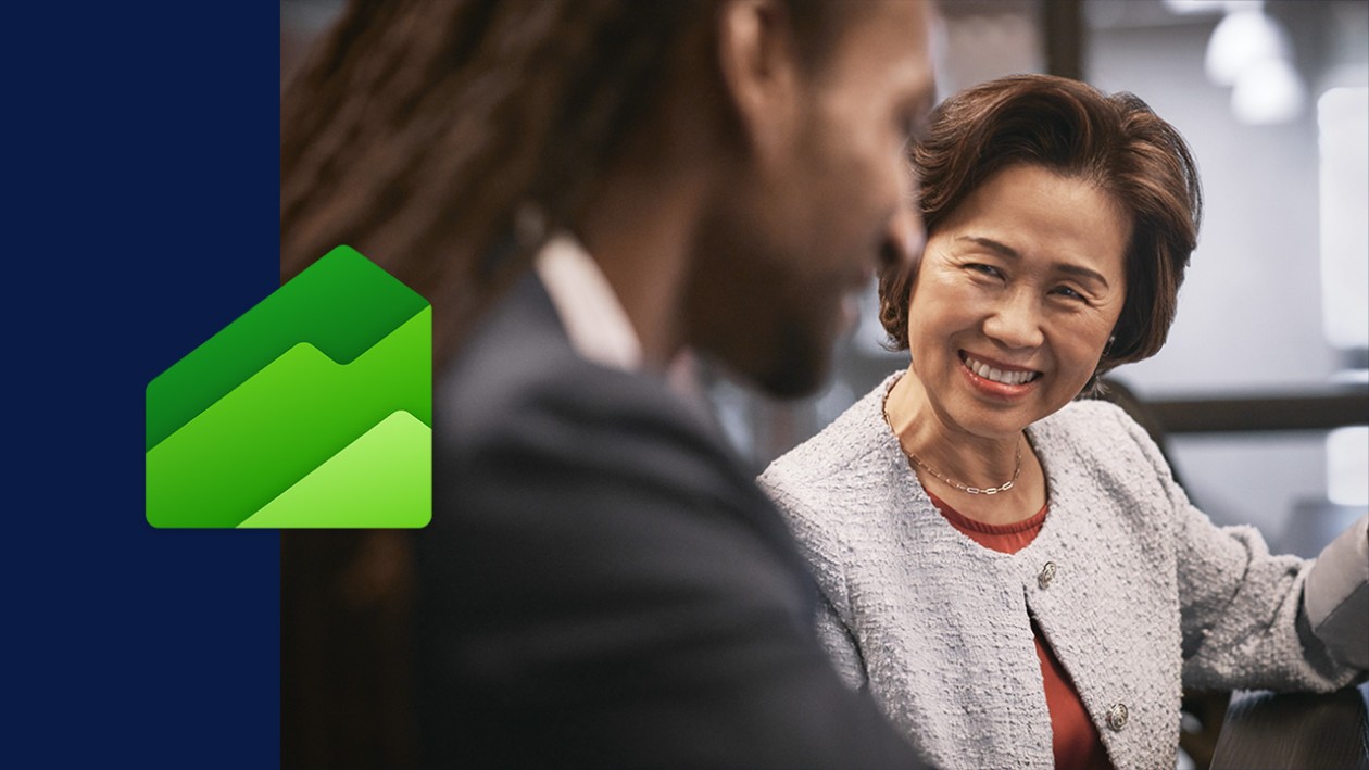 A man and woman smiling in an office setting. Theres a wide dark blue border on the left side of the image with the Dynamics 365 Finance icon overlaid