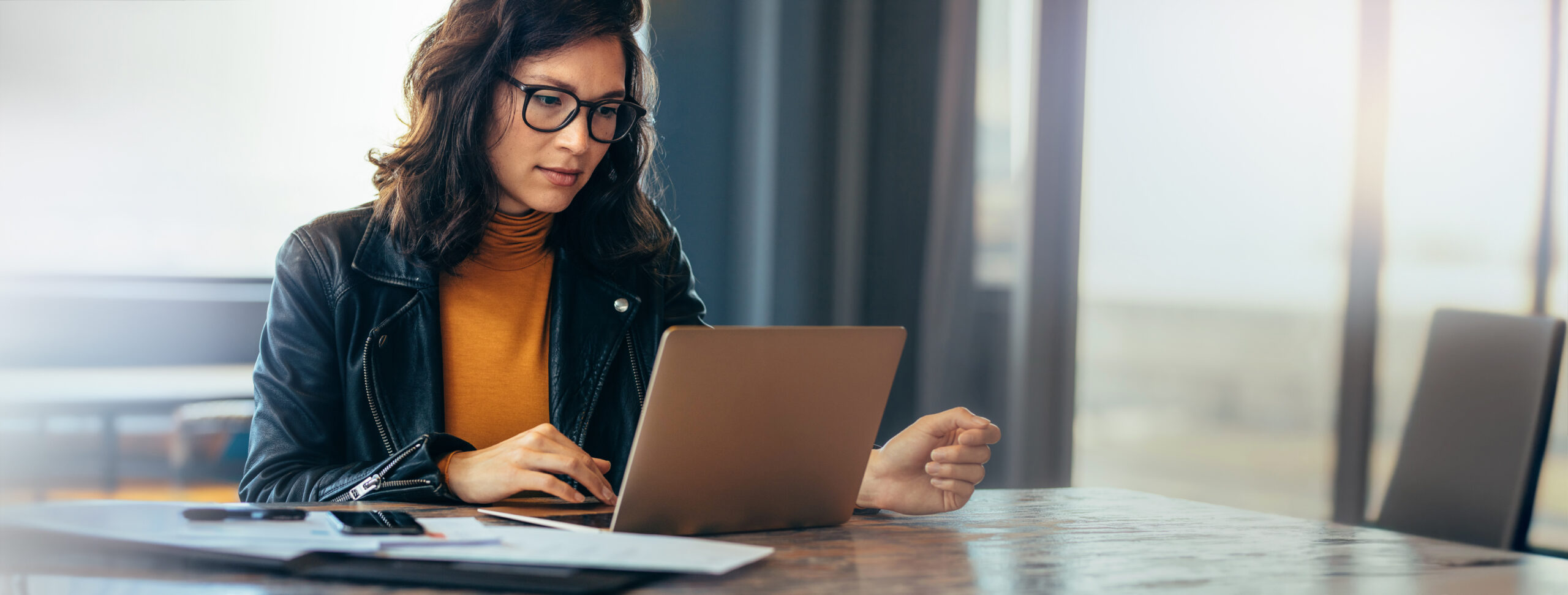 Asian business woman sitting at a table in an office, typing on her laptop with focus. Young female professional showing a dedication and commitment to her project at work