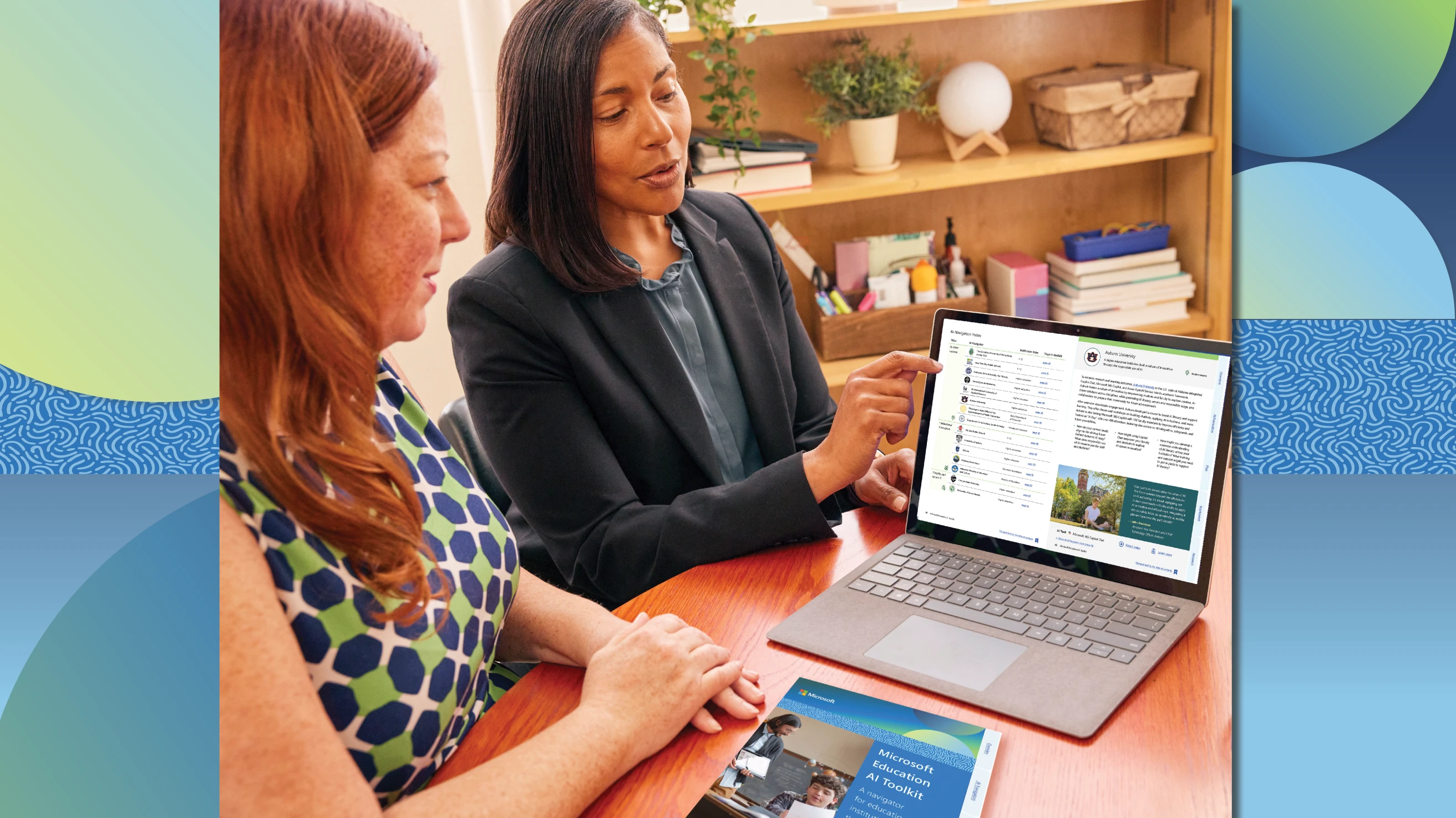 Two education leaders sitting at a table in a school office and looking at the screen of a laptop together