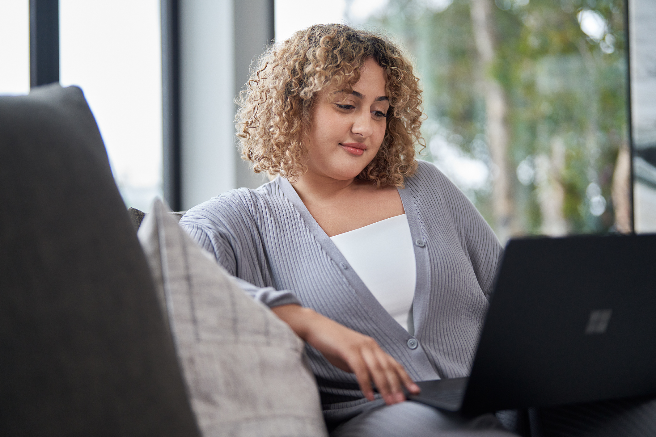 An educator sits on a sofa while looking at a laptop screen