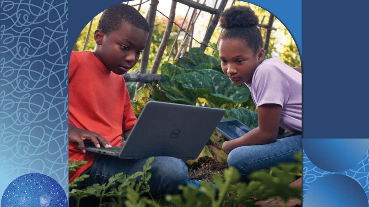 Two students sit in a garden together and work on a project on their laptops