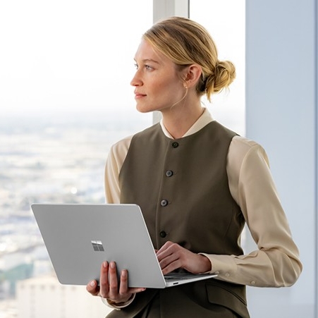 A woman stands and listens while holding an open laptop