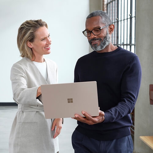 Two people stand together, smiling while they look at a laptop together