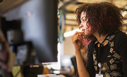 A woman with earbuds in looks at her computer screen