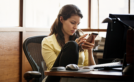 Image of a woman checking her phone while working at her desk