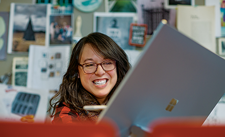 A firstline worker sits behind an open laptop, smiling during a meeting