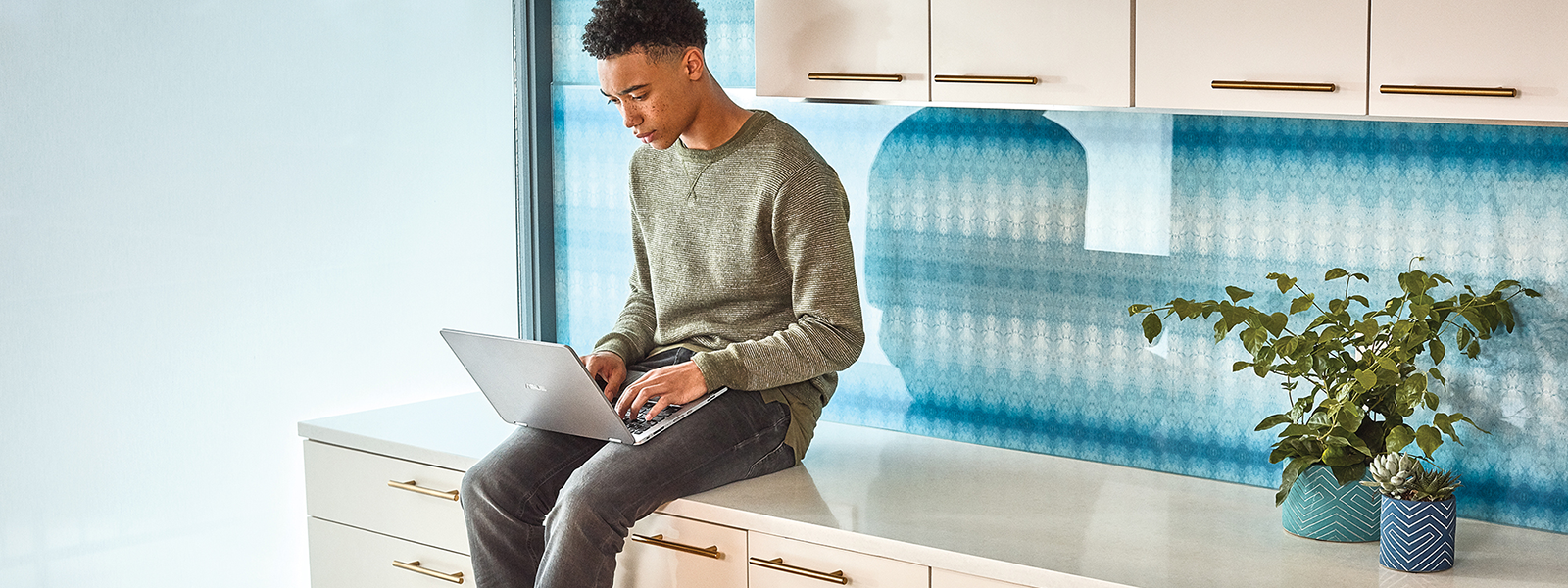 Image of a man sitting on a countertop with a laptop in his lap