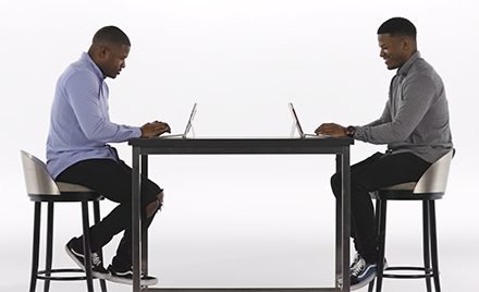 Image of twins sitting at a table, each with a laptop open