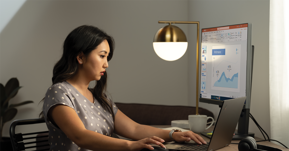 An image of a woman working at her home office on a Lenovo ThinkPad Yoga connected to an external monitor